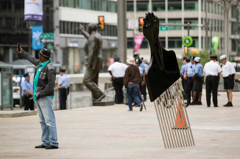 A man takes a selfie with Hank Willis Thomas’ All Power to All People sculpture in view of a statue of former Philadelphia Mayor and Police Commissioner Frank Rizzo in Philadelphia on Sept. 14, 2017.